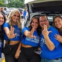 Family poses for picture beside car in parking lot during Family Day tailgate.